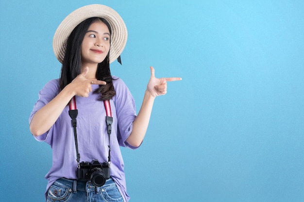 Femme asiatique avec chapeau et caméra pointant quelque chose avec un fond coloré