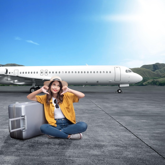 Femme asiatique avec un chapeau et une valise assise avec une expression malheureuse sur la piste