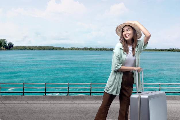 Femme asiatique avec un chapeau et une valise debout dans la rue