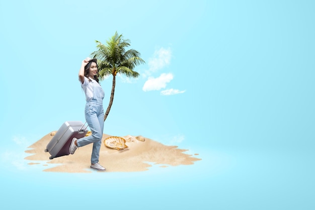 Femme asiatique avec un chapeau et une valise debout sur la plage