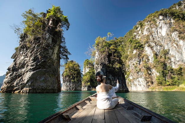 Photo une femme asiatique en chemise blanche est assise devant un bateau avec une belle montagne au milieu de la mer lors d'un voyage en thaïlande. amzing thaïlande.