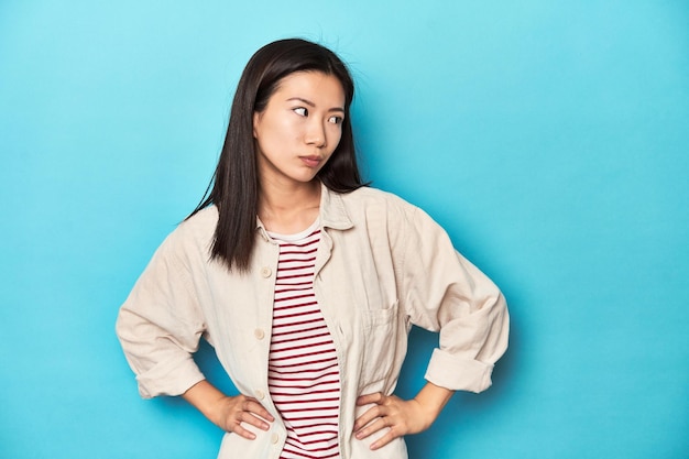 Femme asiatique en chemise superposée et t-shirt rayé confuse se sent dubitative et incertaine