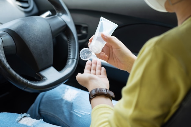 Femme asiatique en chemise verte à l'aide d'un gel d'alcool désinfectant pour les mains se laver et se nettoyer les mains pour prévenir le Covid-19 ou le coronavirus avant de conduire une voiture.