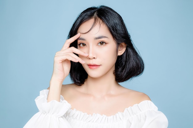 Femme asiatique cheveux courts avec une peau fraîche et propre parfaite Joli modèle féminin avec maquillage naturel et yeux pétillants sur fond bleu isolé Traitement du visage Cosmétologie beauté Concept