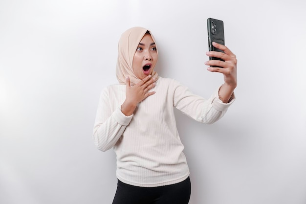 Femme asiatique choquée portant un foulard tenant son téléphone isolé sur fond blanc