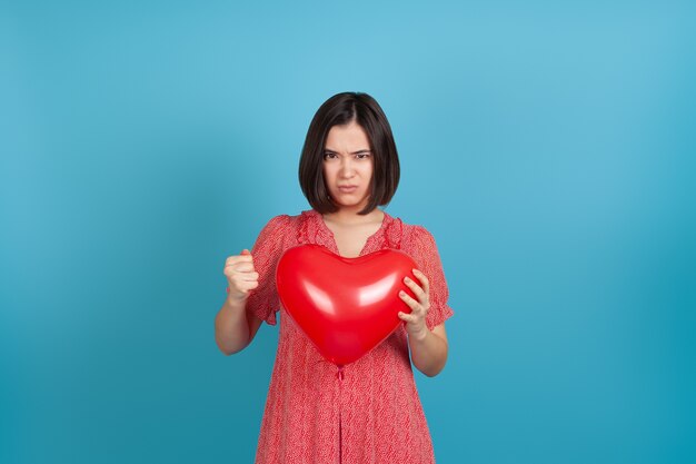 Femme asiatique en colère tenant un ballon coeur rouge et serrant la main dans le poing