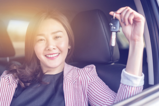 Femme asiatique conducteur souriant et montrant la nouvelle clé de voiture assis dans une voiture