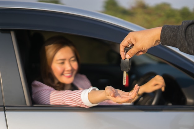 Femme asiatique conducteur souriant et montrant la nouvelle clé de voiture assis dans une voiture