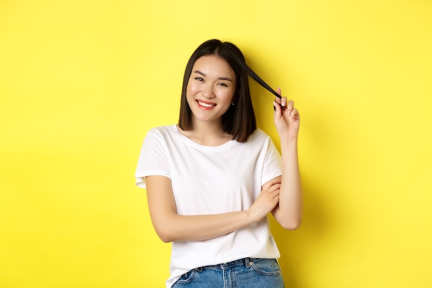 Une femme asiatique confiante et élégante croise les bras sur la poitrine et souriante, debout sur fond jaune