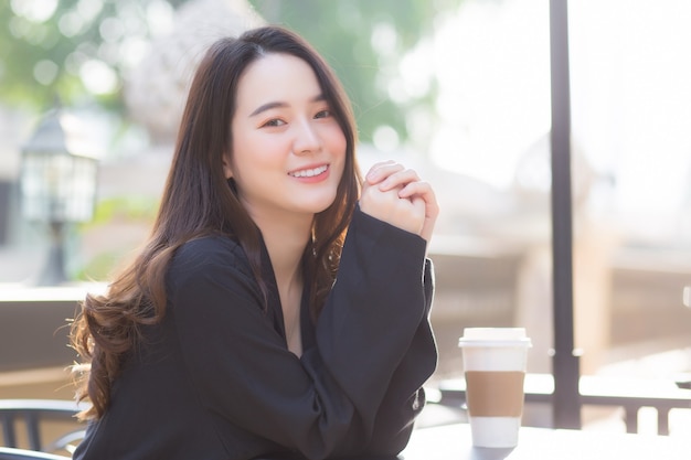 une femme asiatique en costume bleu foncé est assise sur une chaise devant le café par un matin ensoleillé