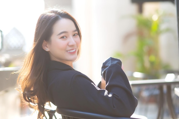 Une femme asiatique en costume bleu foncé est assise sur une chaise et sourit joyeusement devant le café