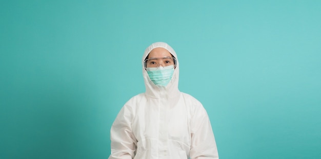 Une femme asiatique en costume EPI porte un masque facial sur fond vert ou bleu Tiffany.