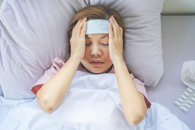 Photo femme asiatique couchée malade à l'aide d'un réducteur de fièvre placé sur le front