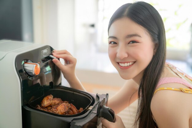 Photo une femme asiatique cuisine du poulet frit en utilisant sa friteuse électrique dans sa cuisine à la maison