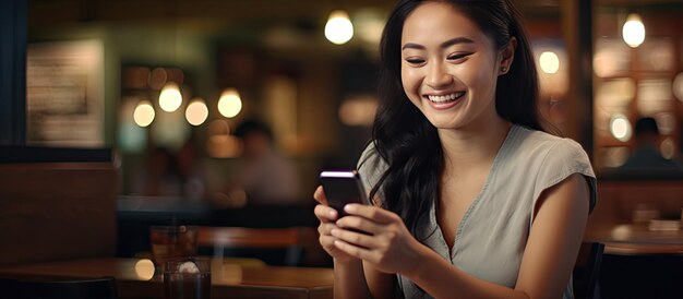 Une femme asiatique dans un restaurant tenant un smartphone avec un écran vide prêt pour un logo de message ou une publicité