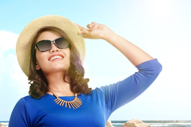 Femme asiatique debout avec chapeau et lunettes de soleil sur la plage avec vue sur le ciel bleu