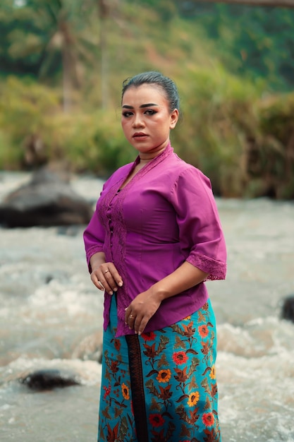 Femme asiatique debout devant la rivière tout en portant une robe violette avec un beau maquillage et une rivière en arrière-plan