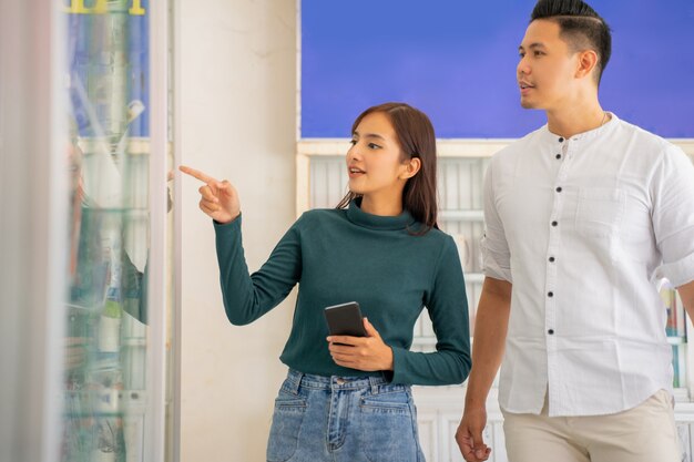 Une femme asiatique debout pointant vers une vitrine en verre tout en choisissant des accessoires pour téléphones portables