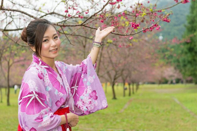 Femme asiatique debout sous le cerisier et levant les mains pour présenter le Sakura et prendre une photo avec.