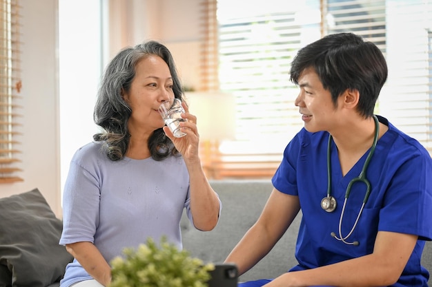 Femme asiatique détendue de 60 ans sirotant de l'eau tout en parlant avec son médecin à la clinique