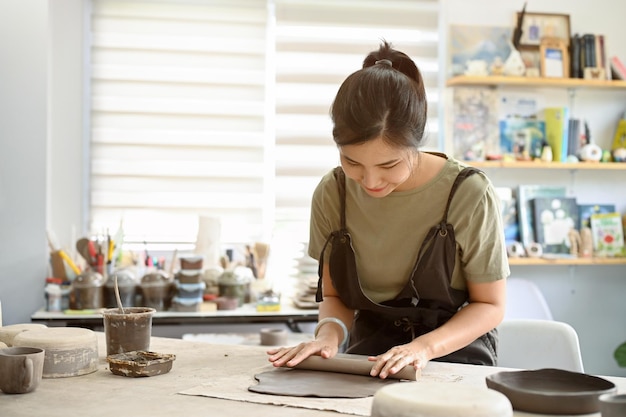 Femme asiatique détendue et calme roulant de l'argile sur une table de travail avec un rouleau d'argile dans l'atelier d'artisanat