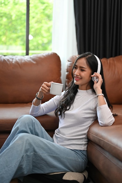 Femme asiatique détendue écoutant de la musique et sirotant un café tout en se relaxant dans le salon