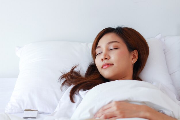 Femme asiatique dort dans un lit blanc en vacances à la maison.