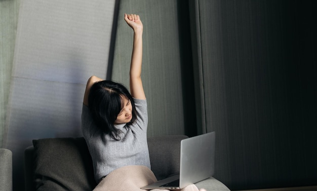 Une femme asiatique a des douleurs à l'épaule en travaillant sur un ordinateur portable à la maison