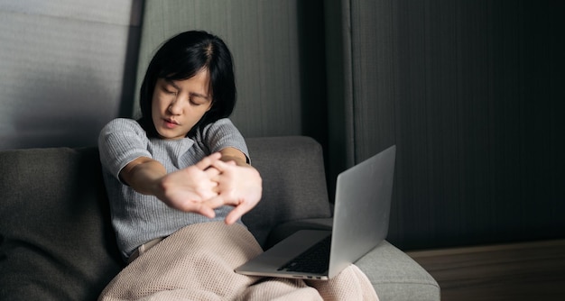 Une femme asiatique a des douleurs à l'épaule en travaillant sur un ordinateur portable à la maison