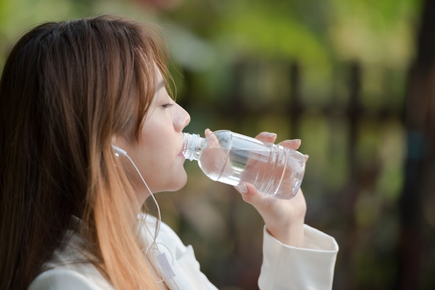 femme asiatique eau potable de la bouteille le matin et écouter de la musique sur fond naturel.