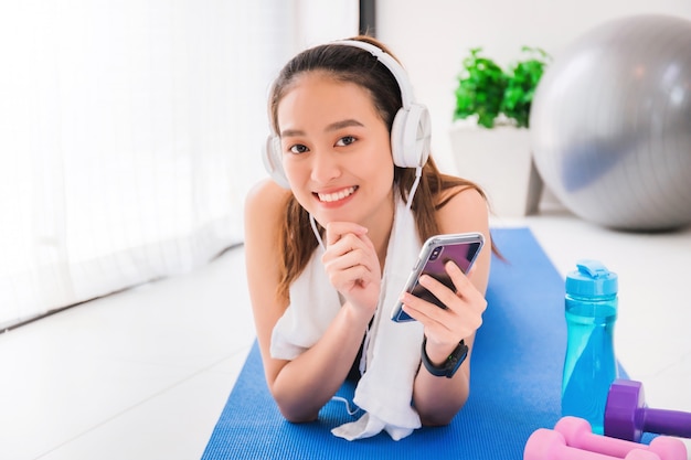 Femme asiatique écoutant de la musique avec casque et smartphone après l'exercice à la maison.