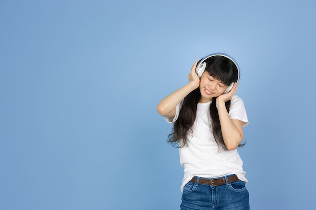 Femme asiatique écoutant de la musique avec des écouteurs sur bleu