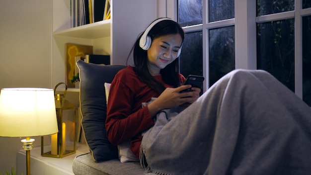 Une femme asiatique écoute de la musique dans le salon la nuit. Style de vie et détente à la maison.