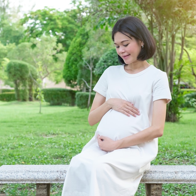 Une femme asiatique enceinte portant des vêtements décontractés assis et regardant son ventre au parc du jardin