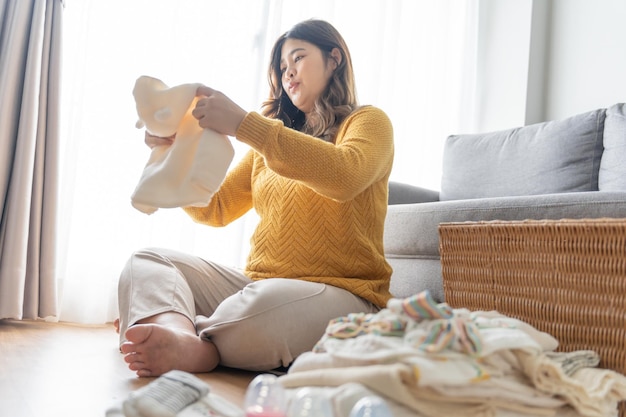 Femme asiatique enceinte se préparant pour la maternité préparant et planifiant les vêtements de bébé pour le nouveau bébé de grossesse, emballant pour la maternité à la maison