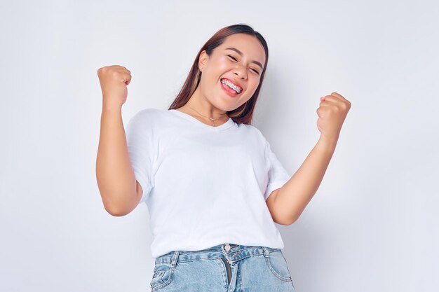 Femme asiatique enthousiaste en t-shirt blanc décontracté se réjouissant de dire oui à l'air heureux et célébrant le geste de pompe de poing de victoire isolé sur fond blanc