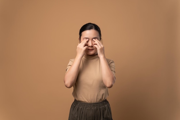 Une femme asiatique était malade de la douleur des yeux irriter les démangeaisons ses yeux debout isolé sur fond beige