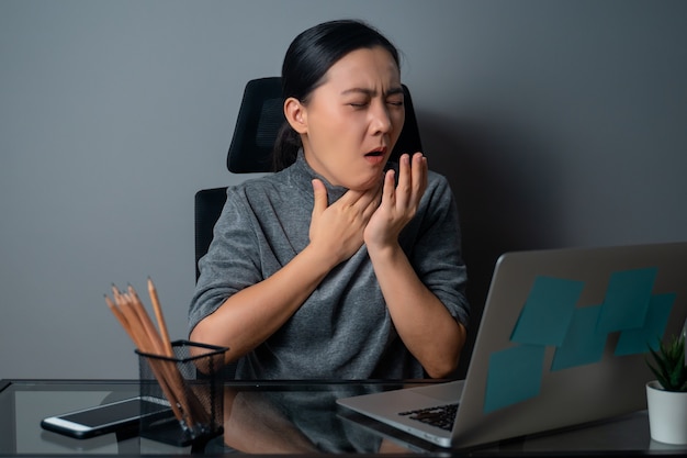 Femme asiatique était malade de fièvre, travaillant sur un ordinateur portable au bureau