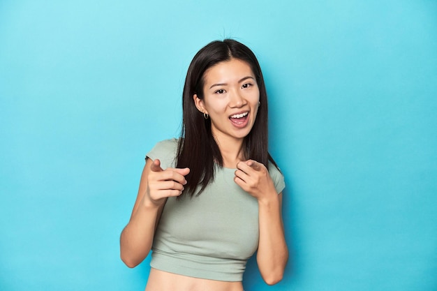 Femme asiatique en été sur fond de studio vert pointant vers l'avant avec les doigts