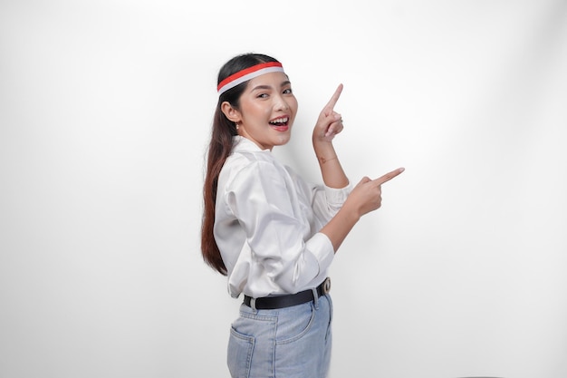 Femme asiatique excitée portant un bandeau de drapeau présentant et pointant vers l'espace de copie sur le côté souriant large et debout sur un fond blanc isolé concept publicitaire du jour de l'indépendance