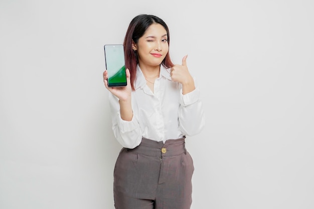 Une femme asiatique excitée portant une chemise blanche donne le pouce en l'air d'un geste d'approbation tout en montrant l'espace de copie sur son téléphone