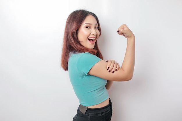 Femme asiatique excitée portant un t-shirt bleu montrant un geste fort en levant les bras et les muscles en souriant fièrement
