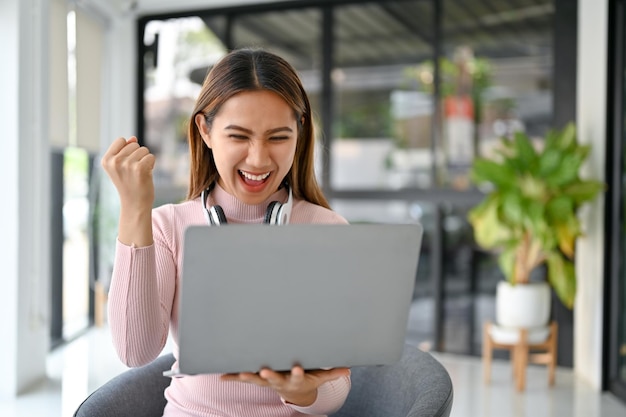 Femme asiatique excitée regardant son écran d'ordinateur portable se réjouissant et hurlant de joie