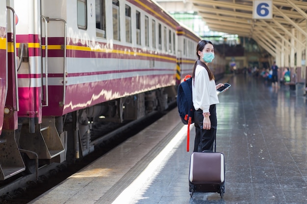 une femme asiatique fait glisser son sac pour voyager ou rentrer chez elle en train à la gare