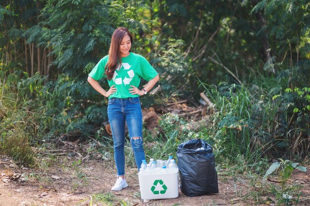 Une femme asiatique finit de ramasser des bouteilles en plastique à ordures dans une corbeille et un sac à l'extérieur