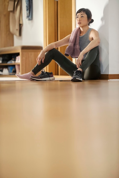 Une femme asiatique en forme d'âge moyen assise sur le sol à la maison et se reposant après des exercices