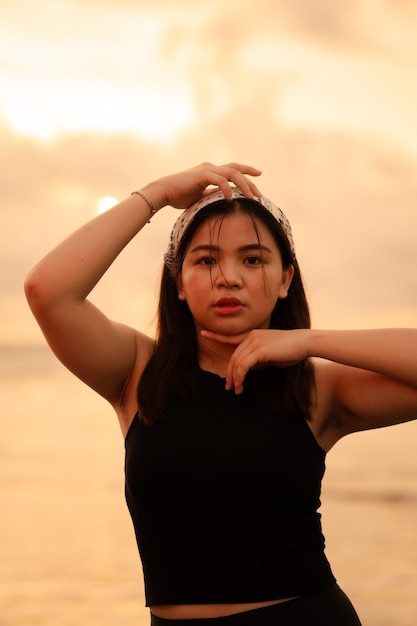 Une femme asiatique glamour en vêtements noirs et un bandana blanc debout devant les vagues sur la plage