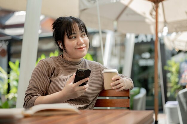 Une femme asiatique heureuse apprécie son café tout en se refroidissant à une table en plein air dans un café