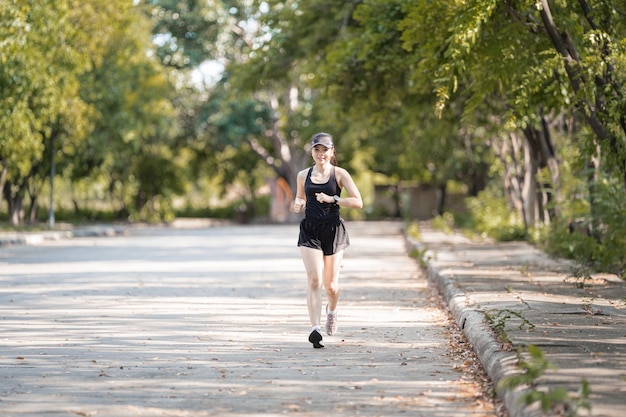 Une femme asiatique heureuse en bonne santé, en tenue de sport noire, faisant du jogging dans le parc naturel de la ville au coucher du soleil