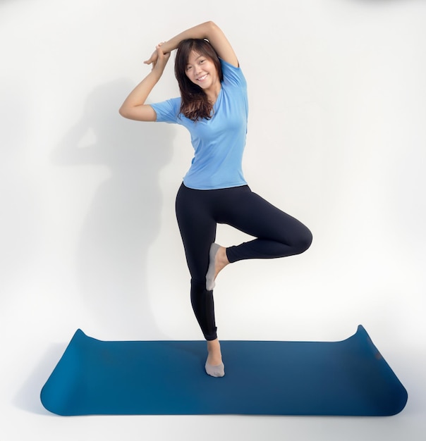 Photo femme asiatique heureuse faire de l'exercice de yoga équilibre debout sur une jambe sur maton de yoga et arrière-plan isolé